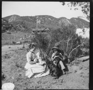 A woman sitting in the dirt with a baby on her lap and a young boy at her side