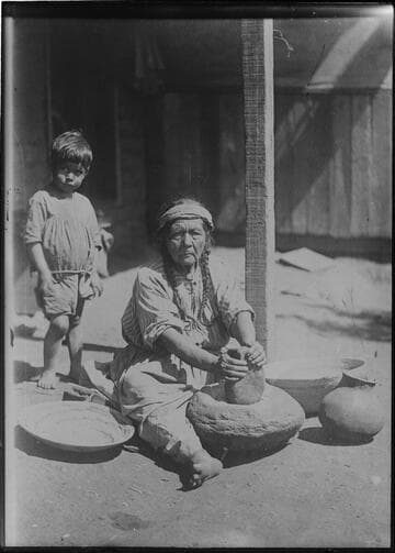 Paiute woman grinding meal on stone mortar (or metate), using stone pestle