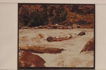 One of the Hatch pontoons carrying two passengers in Hells Half Mile.  The passenger in front is A. J. Johnson.  The oarsman in front is Brick Johnson.  The other oarsman is Dave Rassmussen.  The passenger in the stern