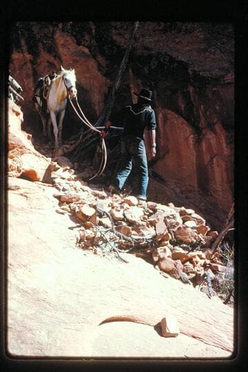 Toby Owl leads his horse on rebuilt trail near mouth of Nasja Creek