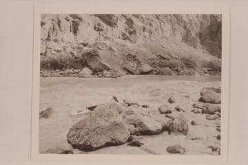 Lining of the Nevills skiffs at Lava Falls.  Nevills is standing in the skiff.  Joe Desloge is helping in shoving the skiff over the rocks.  Kent Frost is snubbing among the rocks at right center