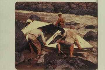 Portage of "Mexican Hat III" at Vulcan Rapid. Duane Bishop is at the stern.  Willard Wright is on the far side.  Frank Wright and Bill Thompson on the near side do not appear to need the safety of a life preserver