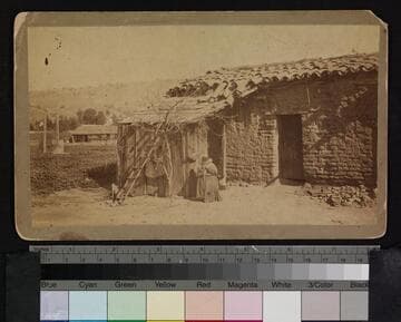Unidentified woman sitting in front of adobe house