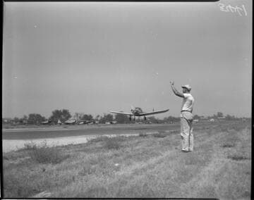 Cessna taking off at airport with man standing next to the runway waving