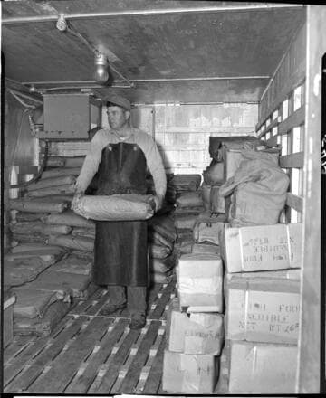 Man storing sacks of ground meat products in cold storage.  Sacks are marked "fish food