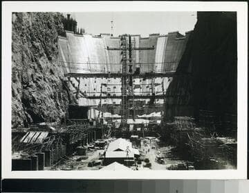 Downstream face of Hoover Dam during construction showing facilities under construction in the de-watered river section