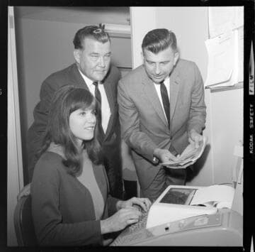 Young lady at keyboard receiving computer data for "House Hunters" from her supervisors