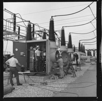 Men working on, or installing large oil circuit-breakers at a transmission substation