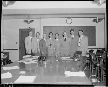 Group of 8 men with one holding an old light bulb