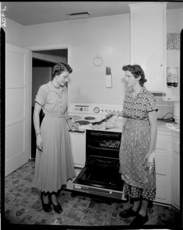 Two women baking muffins in an electric oven