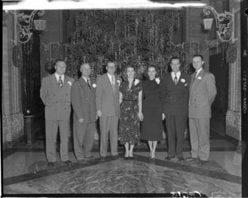 Five men and two women in front of the Christmas tree in the Edison General Office lobby