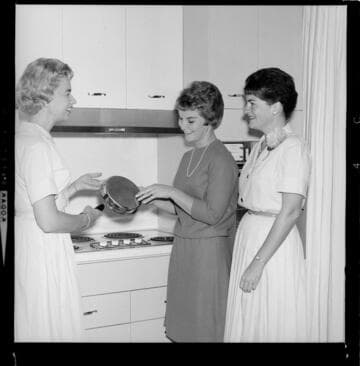 Women demonstrating use and cleaning of electric range coils in teaching kitchen of an electric living center