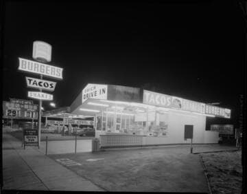 Urich Drive-in Restaurant at night with sign advertising tacos, shakes, and burgers